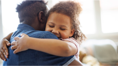 A child hugs her father while smiling in a sunny, well-lit room.