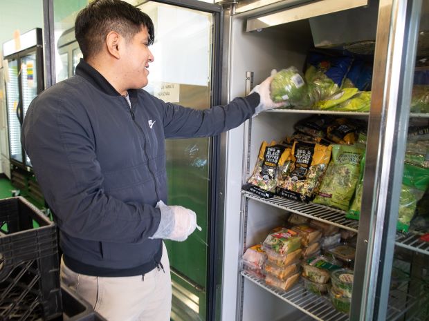A person stocks fresh produce in a refrigerated unit, highlighting food rescue efforts in Hennepin County.