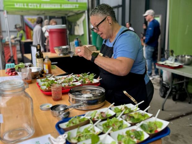 A vendor prepares fresh salad samples at a farmers market stall.