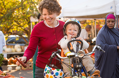 Mom with daughter on a bike picking out food at a farmers market