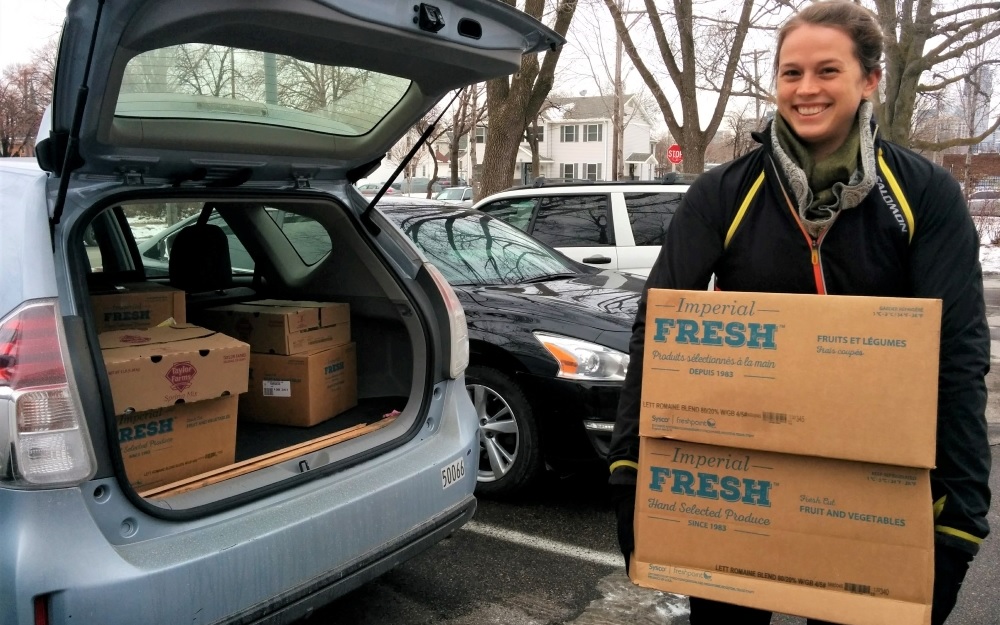 Woman holding boxes of rescued food by open car trunk