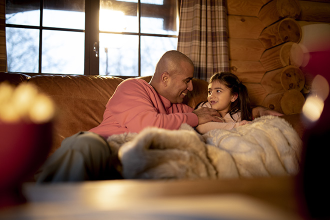 An adult man and his daughter relax on the sofa together.