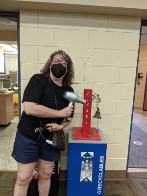 Woman holding hair dryer next to bell that says "Fixed!"
