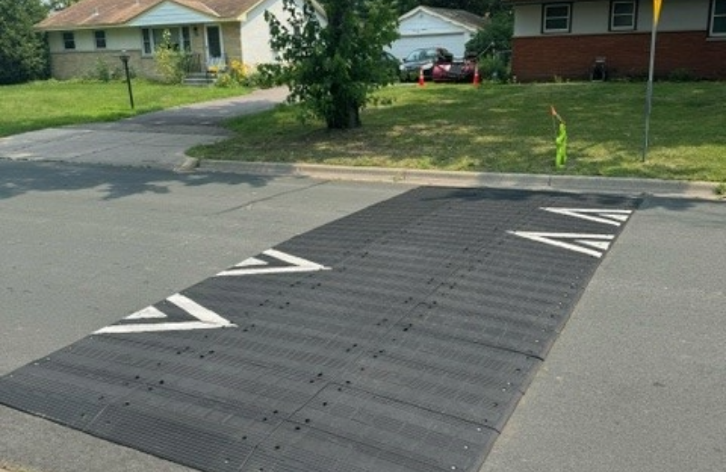 A large black speed bump with white arrow markings spans across a suburban street.