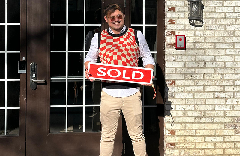 new homeowner standing in front of building with sold sign