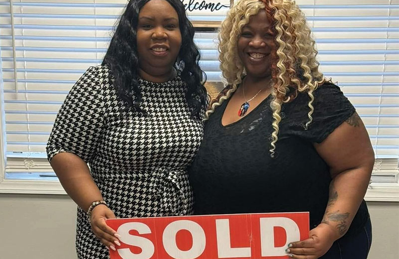 two women inside holding up a sold sign